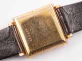 a gold watch with a black leather strap on a white surface