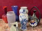 de nombreux vases de toutes sortes posés sur une table, avec un mur rouge en arrière-plan