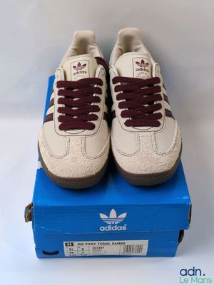 une paire de baskets blanches avec des lacets bordeaux posée sur une boîte bleue