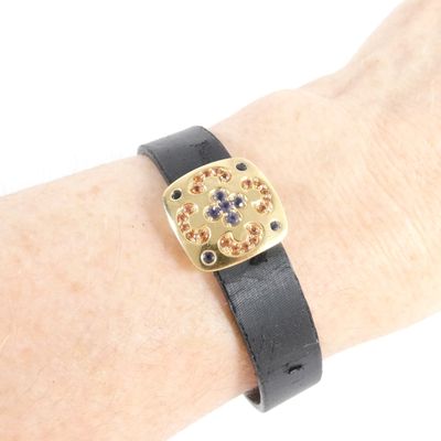 Quelqu'un porte un bracelet en cuir noir orné de pierres dorées et bleues.