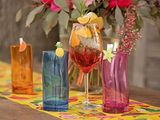 brightly colored glasses and vases sit on a table with flowers in the background