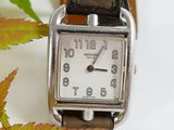 a silver watch with a brown leather band on a white surface