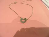 Collier Tiffany avec un cœur vert sur un fond rose, avec l'ombre de la main d'une personne