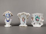 trois vases ornés de motifs floraux sont alignés sur une surface grise