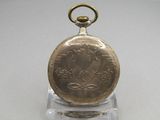 a gold pocket watch on a clear stand on a table