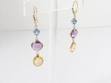 a pair of earrings with multi colored stones on a clear stand