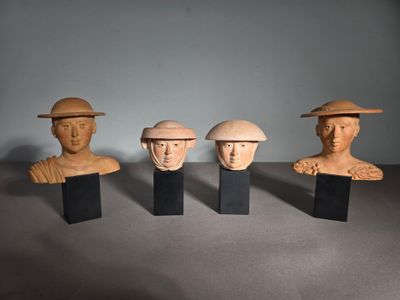trois têtes d'hommes en bois coiffées de chapeaux, posées sur des socles sur une table