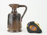 a brown jug and a tape measure on a white surface