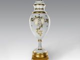un vase blanc et doré posé sur un socle en bois