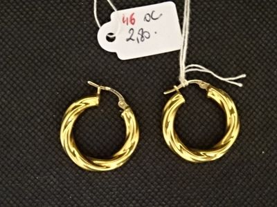 une paire de boucles d'oreilles créoles en or avec une étiquette de prix sur fond noir