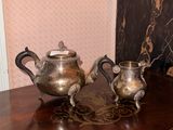 two silver teapots sitting on a table next to a lamp