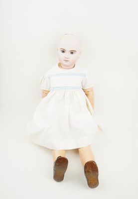 une vieille poupée vêtue d'une robe blanche et de chaussures marron, assise sur une surface blanche
