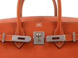 a close up of an orange leather handbag with two metal handles