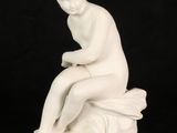 a white statue of a woman sitting on top of a rock