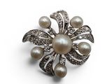 a close up of a pearl and diamond broochle on a white background
