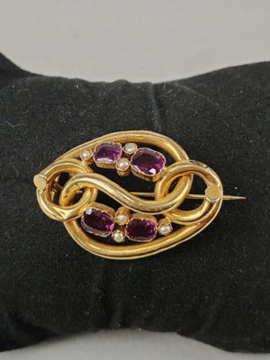 a close up of a gold and purple broochle on a black glove