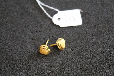 une paire de boucles d'oreilles à clous plaquées or, avec une étiquette de prix posée sur un fond noir