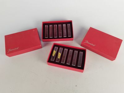 trois boîtes roses contenant des rouges à lèvres, posées sur une surface blanche