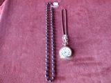 une montre de poche en argent et un collier de perles posés sur un tissu rouge