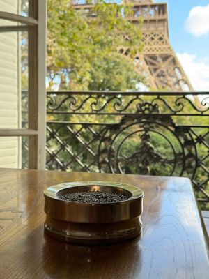 a cup of coffee sitting on a table in front of a window with a view of the eiffel tower
