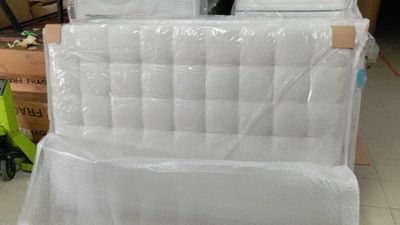 Des cartons contenant des matelas sont empilés les uns sur les autres dans un entrepôt