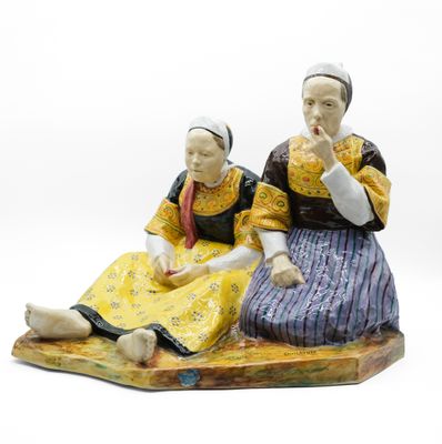 deux figurines représentant deux femmes assises sur un rocher, sur fond blanc