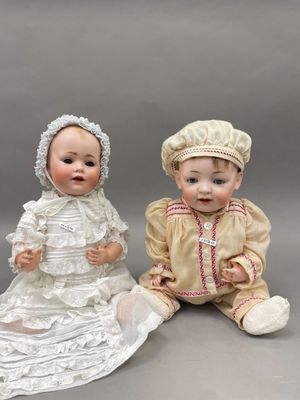 deux poupées en porcelaine représentant des bébés assis l'un à côté de l'autre sur une surface grise