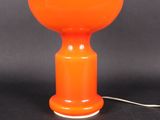 une lampe de table orange avec un cordon blanc posée sur une surface noire