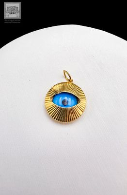 un gros plan d'un pendentif plaqué or orné d'un œil bleu