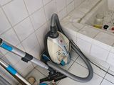 un aspirateur et un balai dans une salle de bains, à côté d'une baignoire