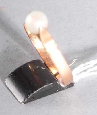 une bague renfermant une perle, posée sur un morceau de métal