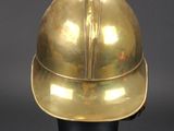 an antique brass helmet on a black stand against a gray background