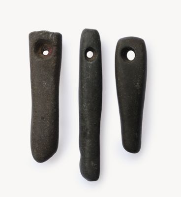 trois pierres noires percées de trous, posées sur une surface blanche