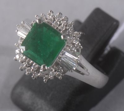 une bague en émeraude et diamants exposée sur un socle noir