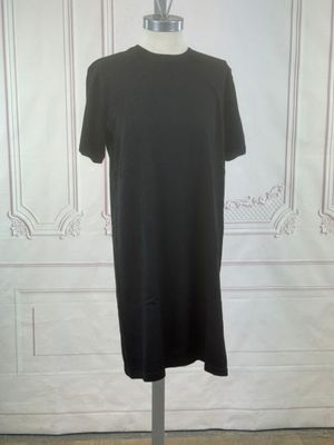 La robe noire est posée sur un mannequin devant un mur blanc.
