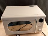 un micro-ondes blanc posé sur une table en bois, avec un cordon noir