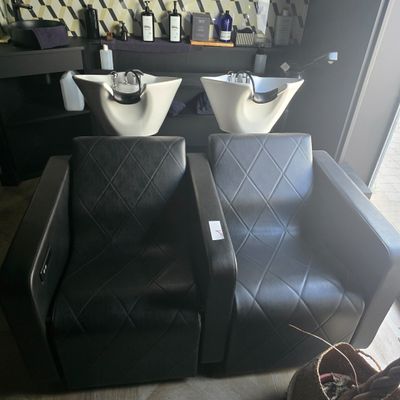 two black chairs in a room with two sinks and a mirror