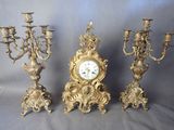 trois chandeliers anciens en laiton et une horloge sur fond gris