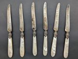 five silverplated knives are lined up on a black surface