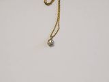 a close up of a gold necklace with a diamond on it