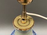 a blue and white vase with a gold lamp on it
