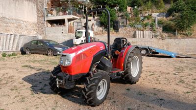 un tracteur rouge garé sur la terre battue