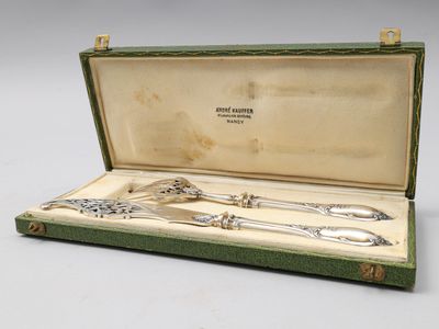 un service d'argenterie ancienne dans un coffret vert posé sur une surface blanche