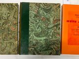 Trois livres sont posés sur une surface blanche ; l'un d'eux a une couverture verte et orange.