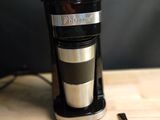 une cafetière noire et argentée posée sur une table en bois, avec une cuillère