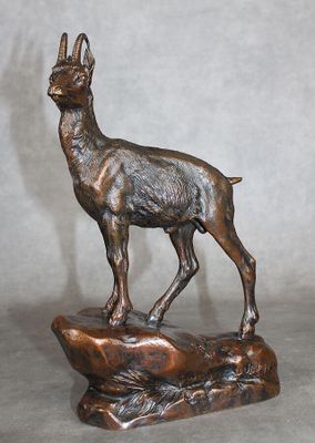 statue en bronze représentant une chèvre posée sur un rocher, sur fond gris