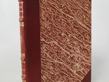 an old book with a red cover sitting on top of a white surface