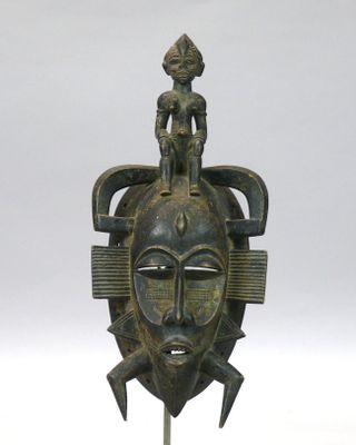 un gros plan d'un masque en bronze posé sur un socle, sur une surface blanche