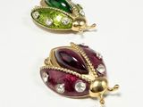 pair of ladybug brooches with green, red, and gold accents