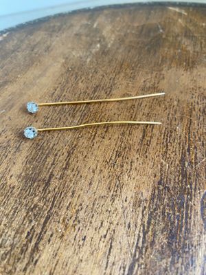 two gold - plated hair pins are sitting on a wooden table